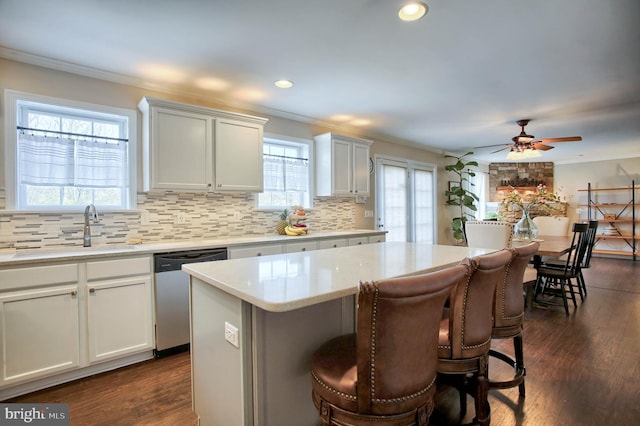 kitchen with stainless steel dishwasher, a sink, crown molding, and a center island