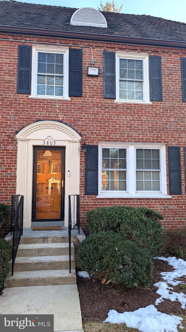 view of exterior entry featuring brick siding and roof with shingles