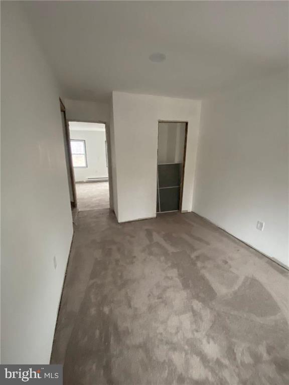 carpeted spare room with a baseboard heating unit