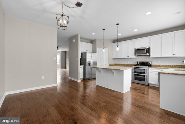 kitchen with pendant lighting, a breakfast bar area, appliances with stainless steel finishes, white cabinets, and dark hardwood / wood-style flooring