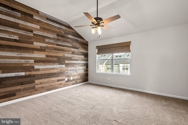 carpeted spare room featuring wooden walls, ceiling fan, and vaulted ceiling