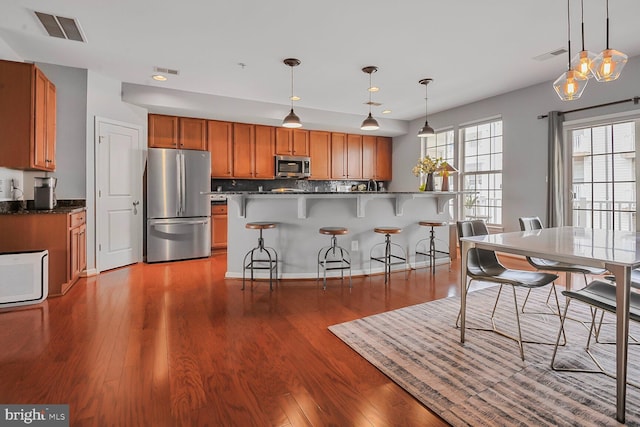 kitchen featuring a kitchen bar, tasteful backsplash, wood-type flooring, pendant lighting, and stainless steel appliances