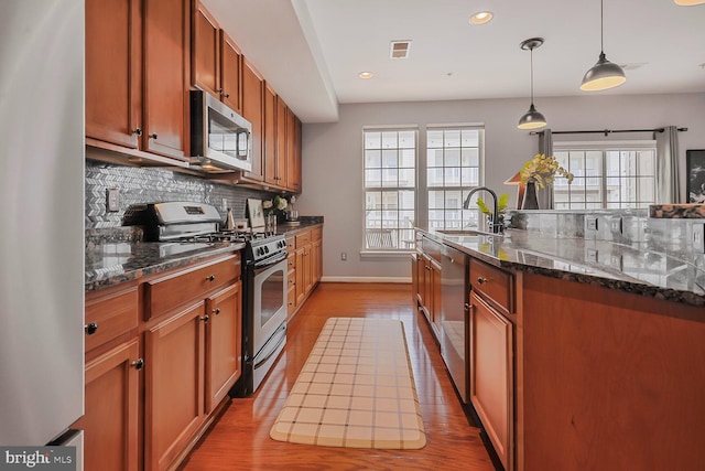 kitchen featuring sink, decorative light fixtures, dark stone countertops, stainless steel appliances, and backsplash