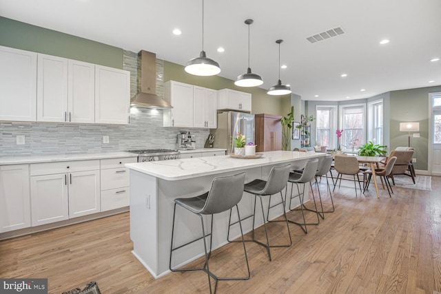 kitchen featuring a center island, visible vents, freestanding refrigerator, decorative backsplash, and wall chimney exhaust hood