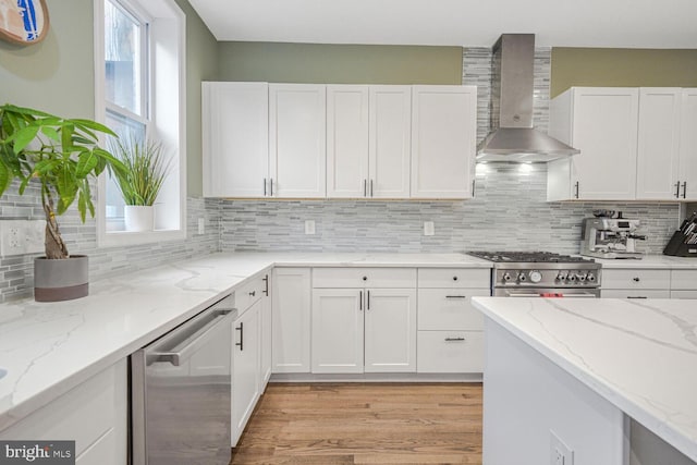 kitchen featuring white cabinetry, wall chimney range hood, appliances with stainless steel finishes, light stone countertops, and tasteful backsplash