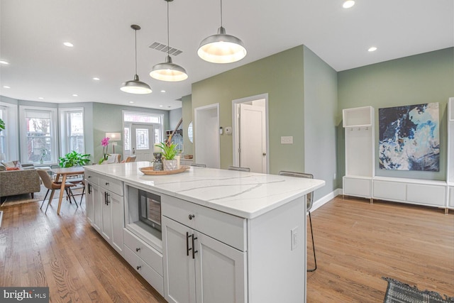 kitchen featuring light stone counters, visible vents, open floor plan, hanging light fixtures, and light wood finished floors