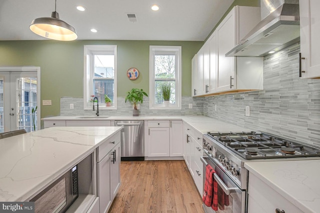 kitchen with a sink, white cabinets, french doors, wall chimney range hood, and appliances with stainless steel finishes