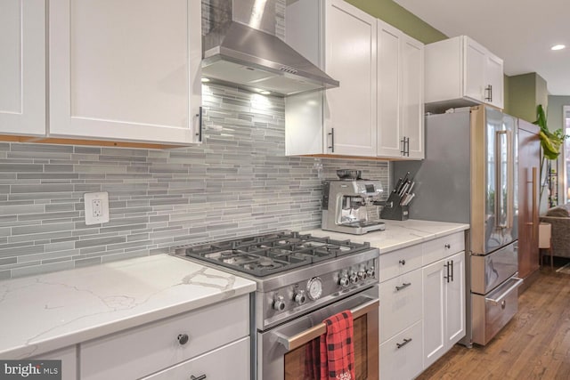 kitchen featuring wall chimney range hood, white cabinetry, appliances with stainless steel finishes, and backsplash