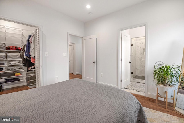 bedroom with baseboards, wood finished floors, a walk in closet, a closet, and recessed lighting