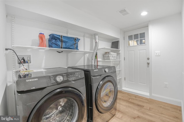 clothes washing area with laundry area, visible vents, baseboards, wood finished floors, and washing machine and dryer