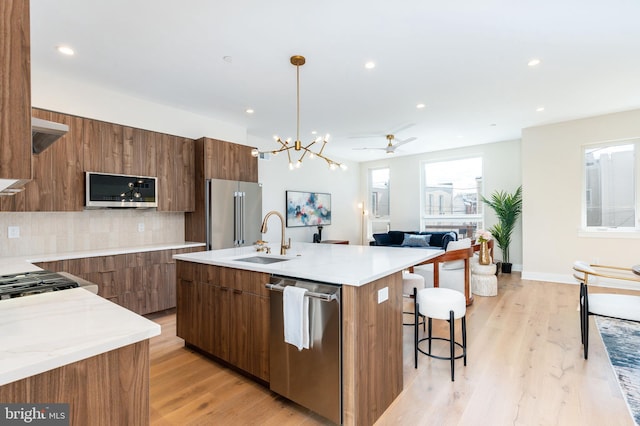 kitchen with sink, hanging light fixtures, a center island with sink, stainless steel appliances, and decorative backsplash