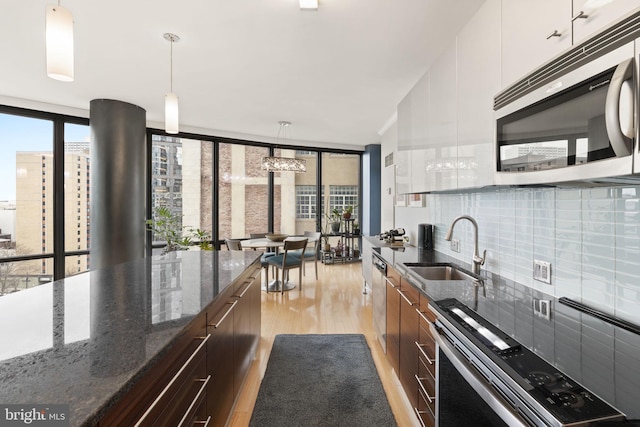 kitchen with a sink, white cabinetry, appliances with stainless steel finishes, modern cabinets, and decorative light fixtures