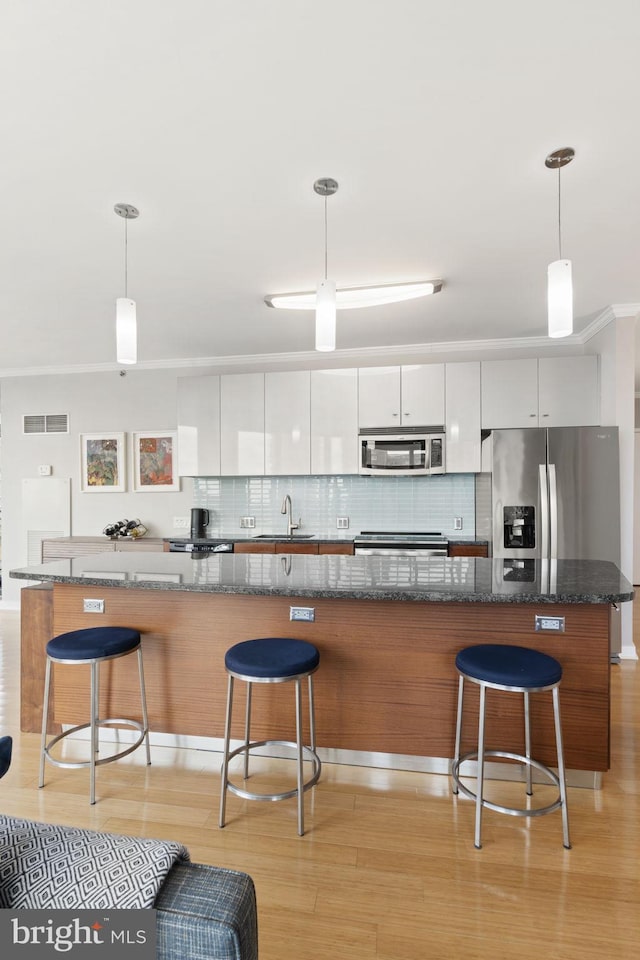 kitchen featuring appliances with stainless steel finishes, modern cabinets, white cabinetry, and decorative light fixtures