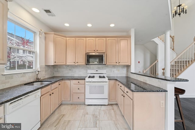 kitchen featuring white appliances, visible vents, a peninsula, light brown cabinets, and a sink