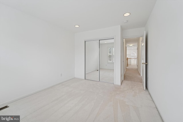 unfurnished bedroom with recessed lighting, a closet, light colored carpet, and visible vents