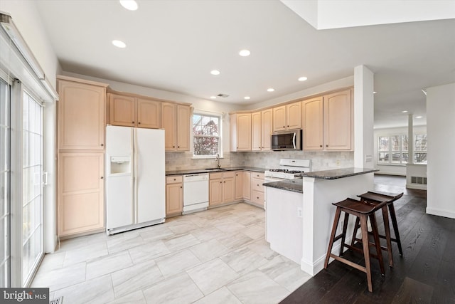 kitchen featuring light brown cabinets, a peninsula, white appliances, a sink, and backsplash