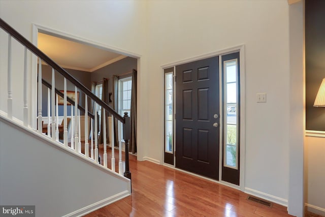 foyer with wood finished floors, visible vents, baseboards, stairs, and ornamental molding