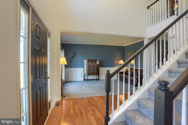 foyer with visible vents, a decorative wall, ornamental molding, wainscoting, and wood finished floors