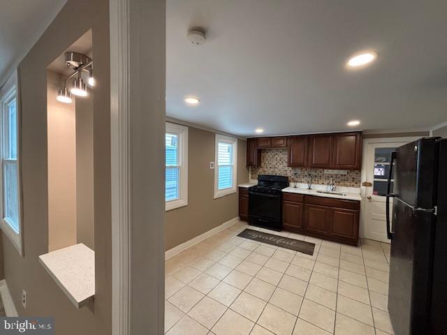 kitchen featuring tasteful backsplash, sink, light tile patterned floors, and black appliances