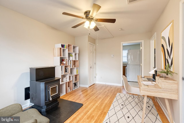 office featuring light hardwood / wood-style floors, ceiling fan, and a wood stove