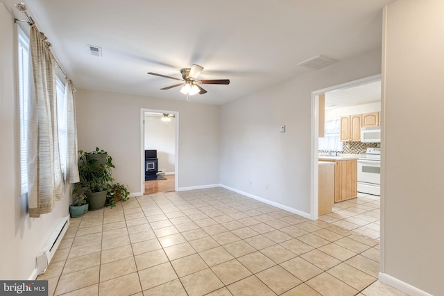 tiled empty room with a wood stove, ceiling fan, and baseboard heating