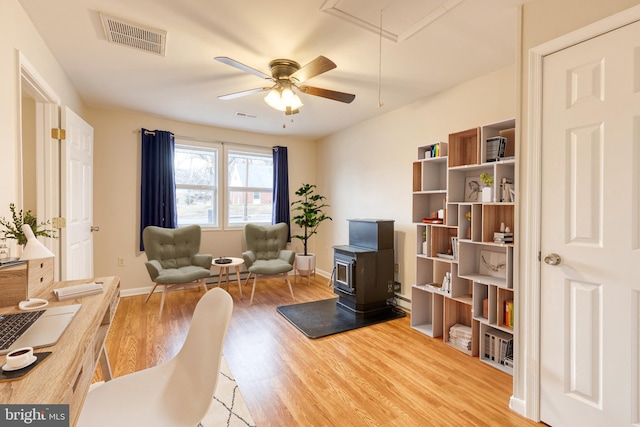 living area with wood-type flooring, ceiling fan, and a wood stove