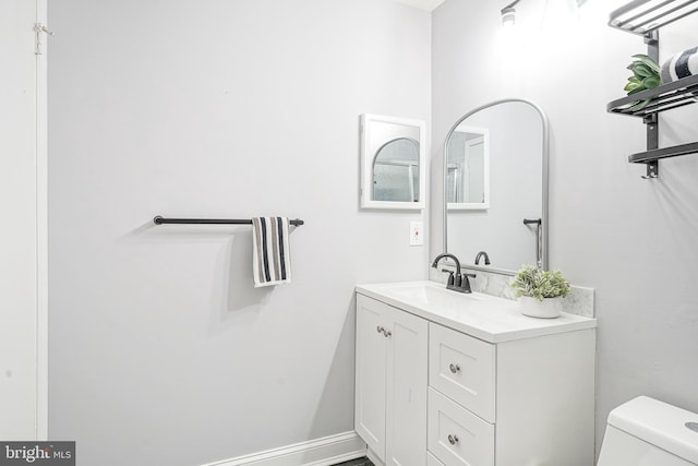 half bath featuring baseboards, vanity, and toilet