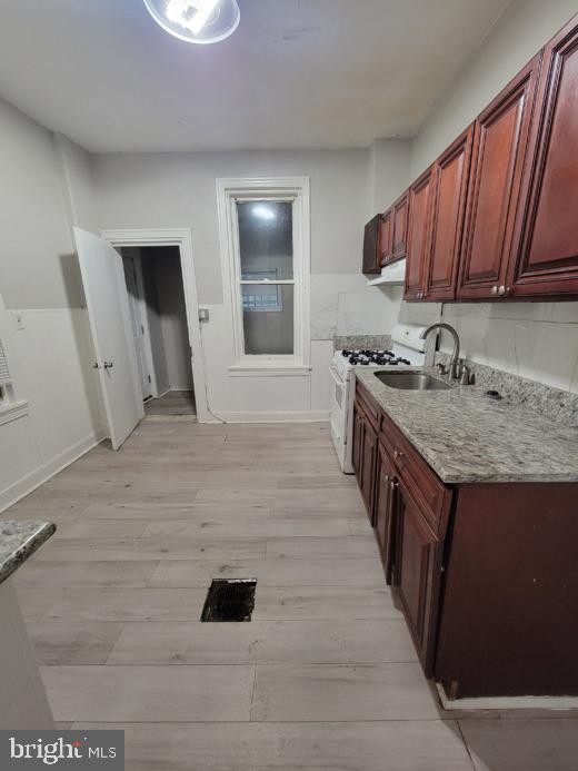 kitchen featuring sink, light stone countertops, light hardwood / wood-style floors, and gas range gas stove