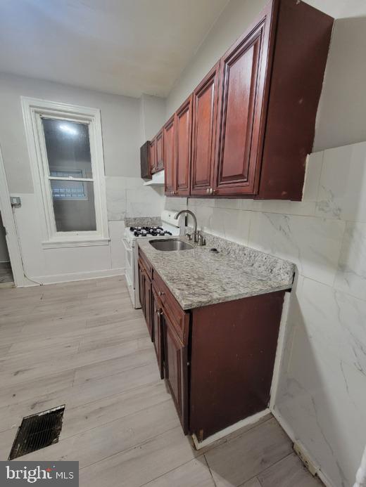 kitchen with light stone counters, sink, white gas range, and light hardwood / wood-style floors