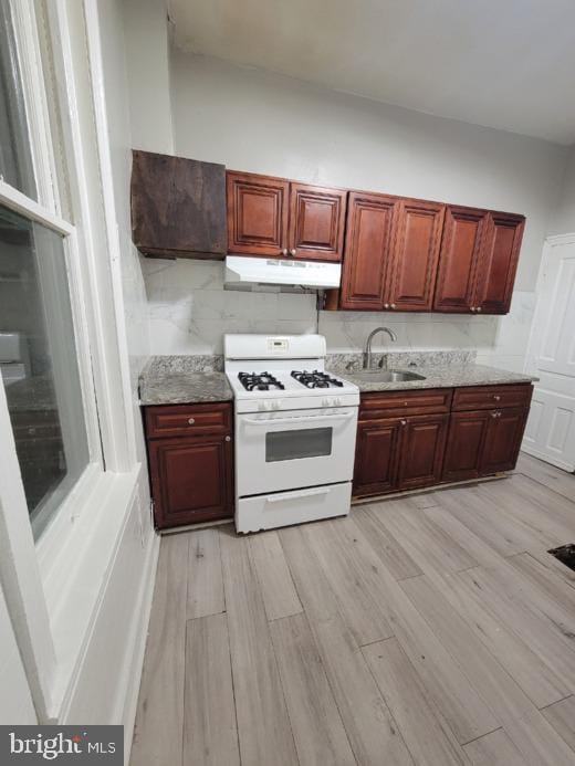 kitchen with sink, light hardwood / wood-style floors, white gas range oven, and light stone countertops