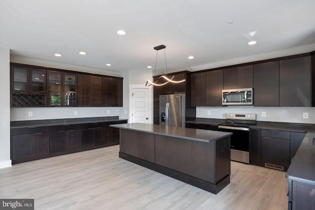 kitchen featuring decorative light fixtures, a center island, stainless steel appliances, dark brown cabinets, and light hardwood / wood-style flooring