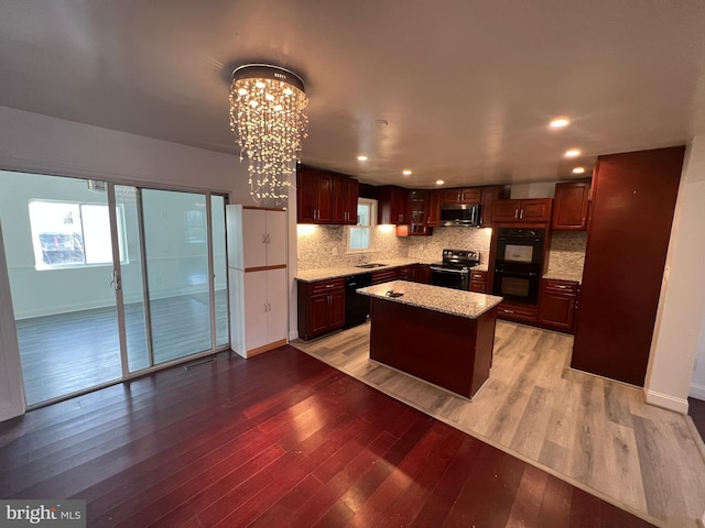 kitchen featuring a kitchen island, tasteful backsplash, black appliances, an inviting chandelier, and light hardwood / wood-style flooring