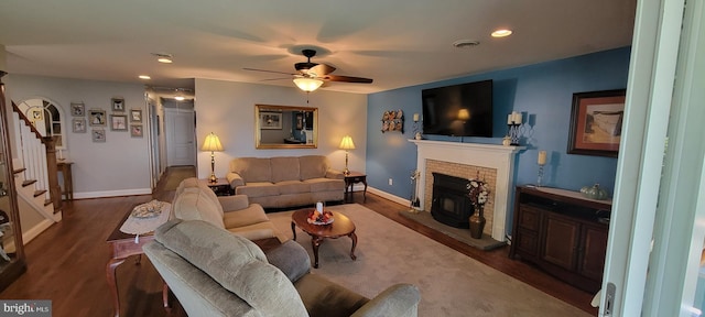 living room with ceiling fan, a fireplace, wood finished floors, visible vents, and stairway