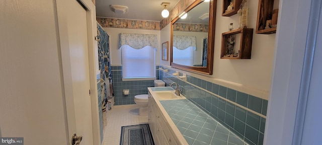 full bathroom with wainscoting, toilet, tile patterned flooring, vanity, and tile walls