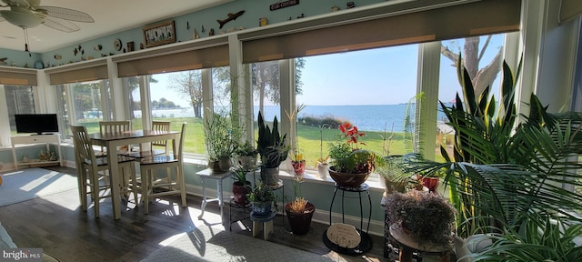 sunroom with plenty of natural light, a ceiling fan, and a water view