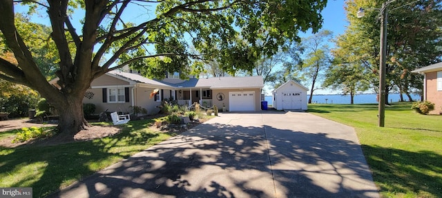 ranch-style house featuring concrete driveway, a front lawn, an attached garage, and a water view