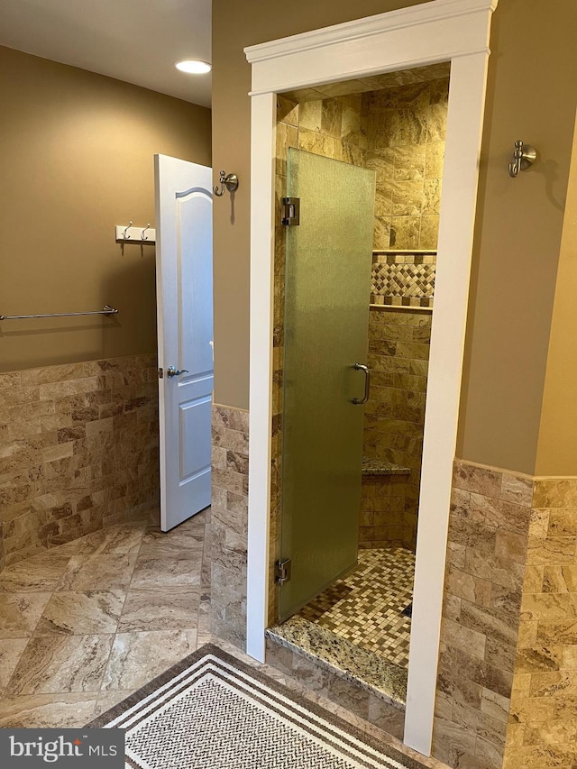 bathroom with a wainscoted wall, a shower stall, and tile walls