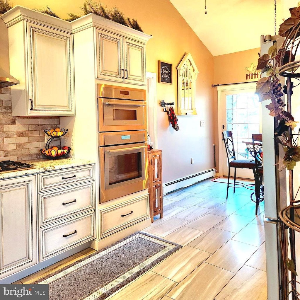 kitchen featuring stainless steel appliances, cream cabinets, a baseboard radiator, and decorative backsplash