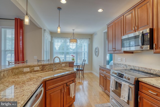 kitchen featuring stainless steel appliances, hanging light fixtures, a sink, and brown cabinets