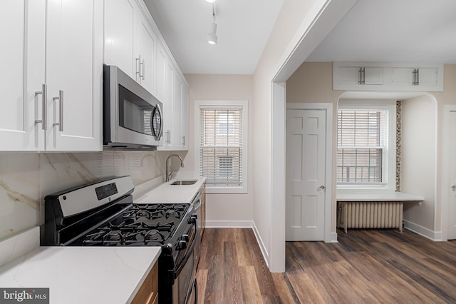 kitchen featuring radiator, sink, white cabinets, stainless steel appliances, and light stone countertops