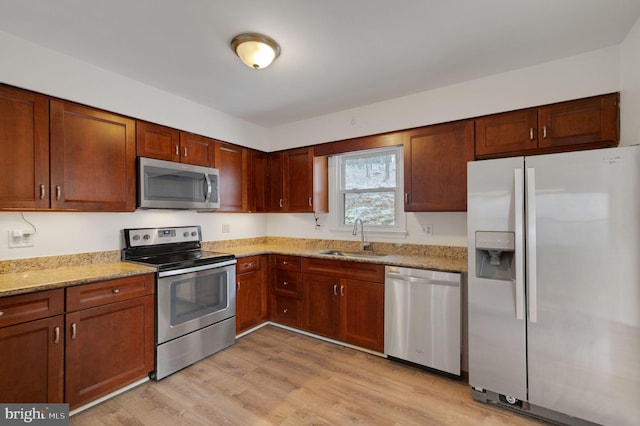 kitchen featuring light stone counters, light wood-style flooring, stainless steel appliances, a sink, and brown cabinets