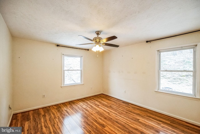 empty room featuring plenty of natural light, a textured ceiling, baseboards, and wood finished floors