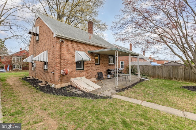 rear view of property featuring a chimney, fence, brick siding, a lawn, and a patio