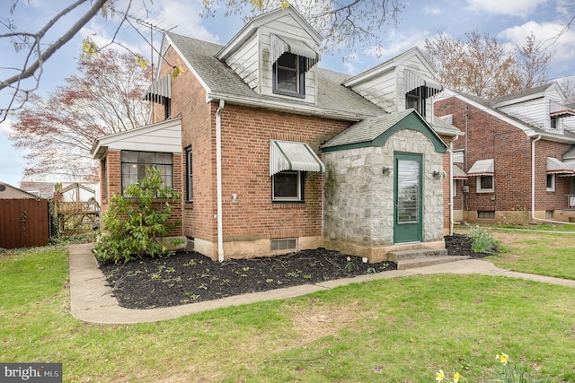 cape cod home featuring roof with shingles, fence, brick siding, entry steps, and a front yard