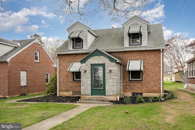 cape cod-style house with entry steps, brick siding, a front yard, and roof with shingles