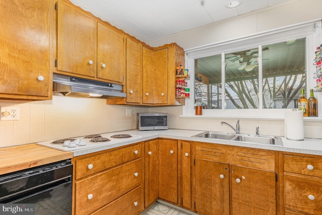 kitchen with a sink, white electric stovetop, light countertops, stainless steel microwave, and under cabinet range hood