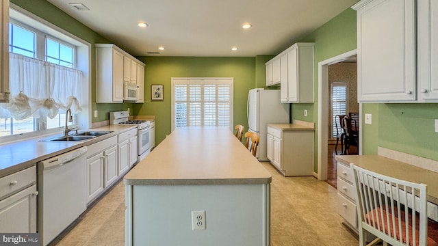 kitchen featuring a center island, white appliances, white cabinets, and a sink