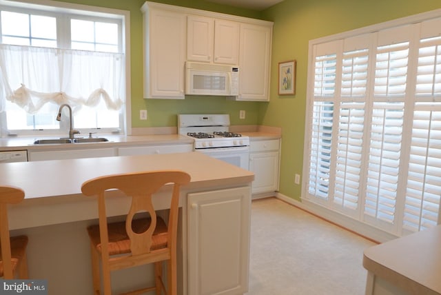 kitchen featuring light floors, light countertops, white cabinetry, a sink, and white appliances