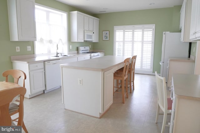 kitchen with white appliances, white cabinets, a kitchen island, light countertops, and a sink