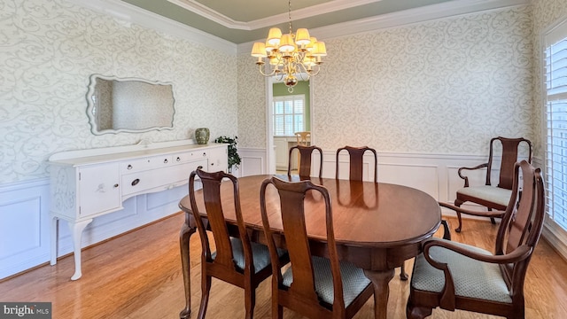 dining space featuring light wood-style floors, a wainscoted wall, ornamental molding, and wallpapered walls